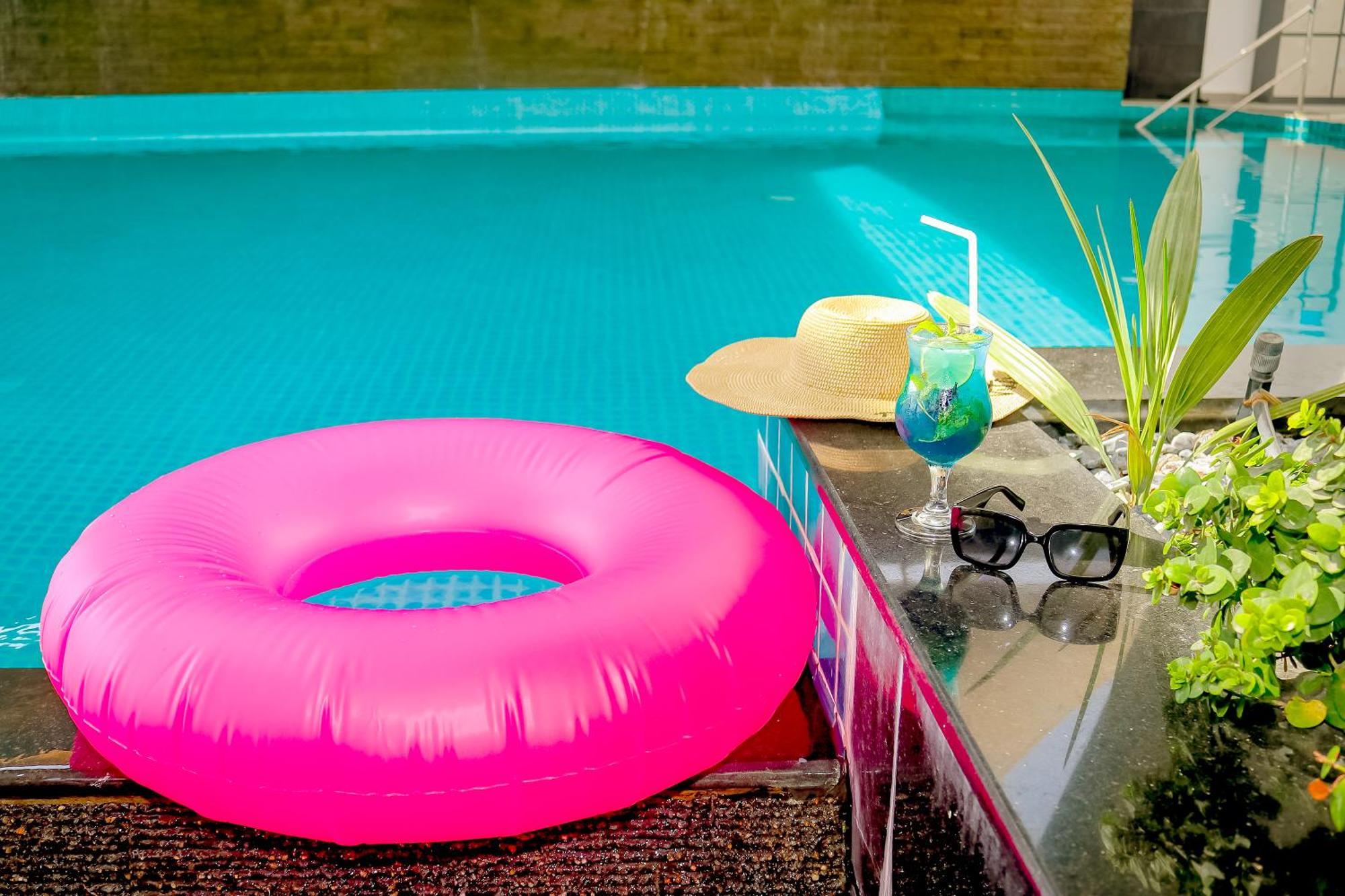 泻湖畔豪华spa度假村 麦纳麦 外观 照片 The photo shows a vibrant and inviting scene by a swimming pool. In the foreground, there is a large pink inflatable float and a stylish straw hat. Next to the float, a refreshing cocktail in a glass is displayed, complete with a straw and garnishes.