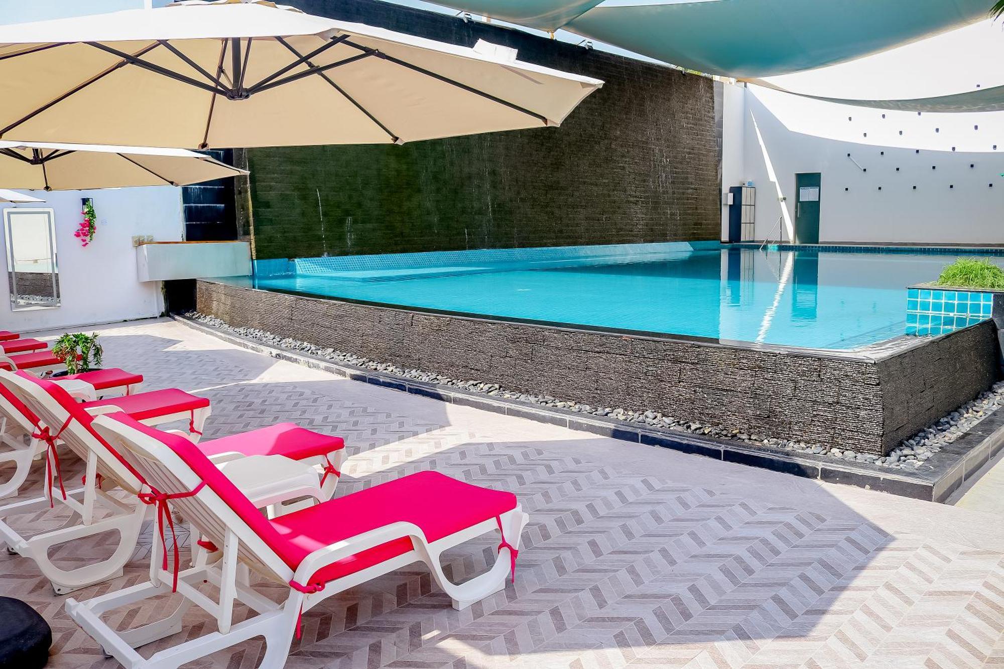 泻湖畔豪华spa度假村 麦纳麦 外观 照片 The photo shows a pool area featuring a rectangular swimming pool with clear blue water. Surrounding the pool are light-colored lounge chairs with pink cushions, positioned under large umbrellas for shade. The pool is bordered by a textured wall, and