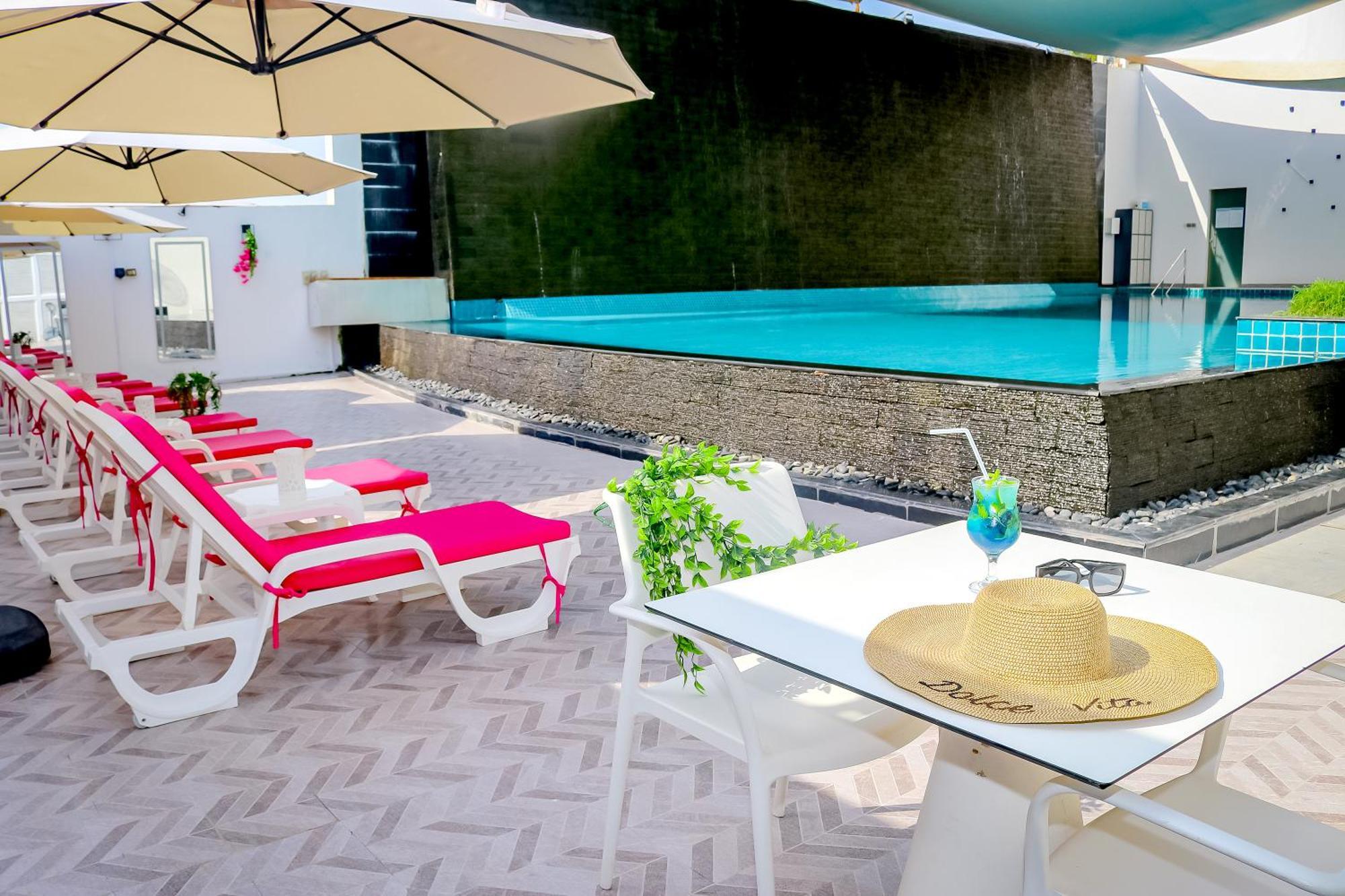 泻湖畔豪华spa度假村 麦纳麦 外观 照片 The photo shows a sunny poolside area with bright red lounge chairs arranged neatly beside a swimming pool. There are large beige umbrellas providing shade. A small table is set up with a straw hat and a colorful drink, suggesting a relaxed, tropical