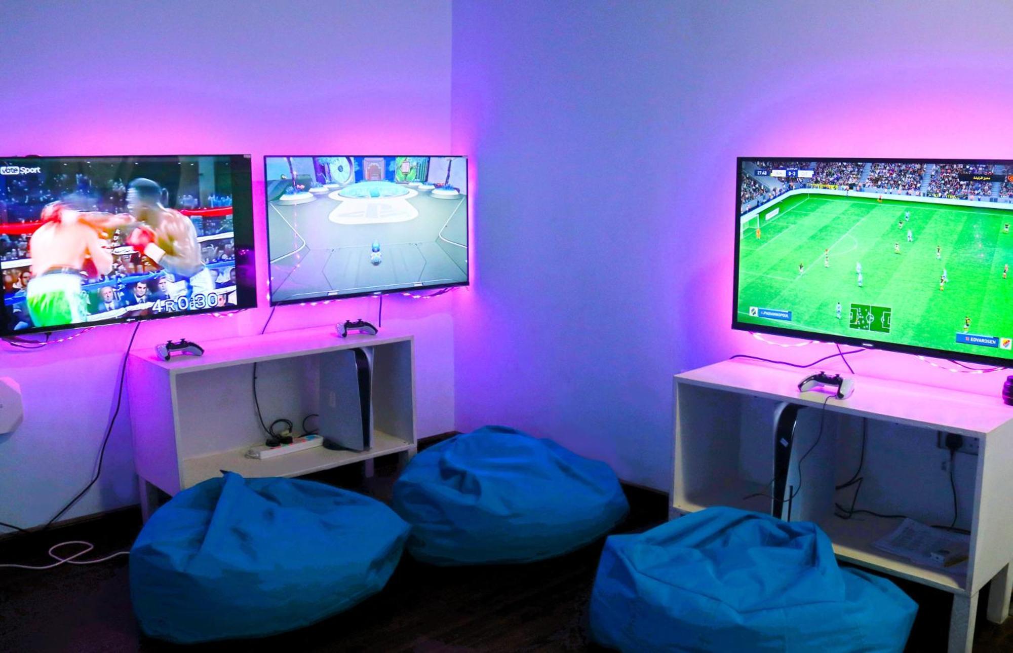 泻湖畔豪华spa度假村 麦纳麦 外观 照片 The photo shows a gaming area featuring three televisions mounted on the wall, displaying different games. Two of the TVs are showing gaming scenes, with one depicting a boxing game and the other showing a vibrant game environment. The third TV displ