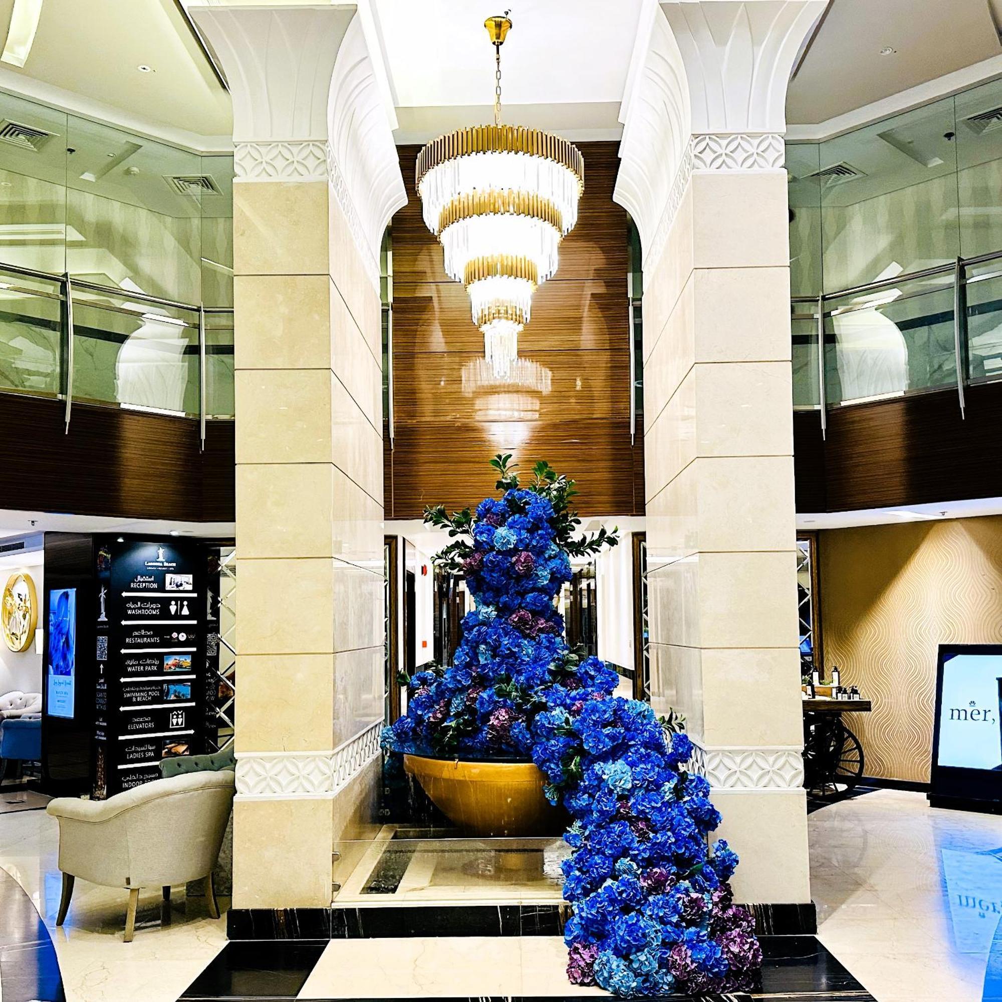 泻湖畔豪华spa度假村 麦纳麦 外观 照片 The photo depicts an elegant lobby or entrance area of a building. Central to the scene is a large floral arrangement featuring vibrant blue flowers. This arrangement is positioned in a decorative bowl. Above it hangs a stylish chandelier with a laye