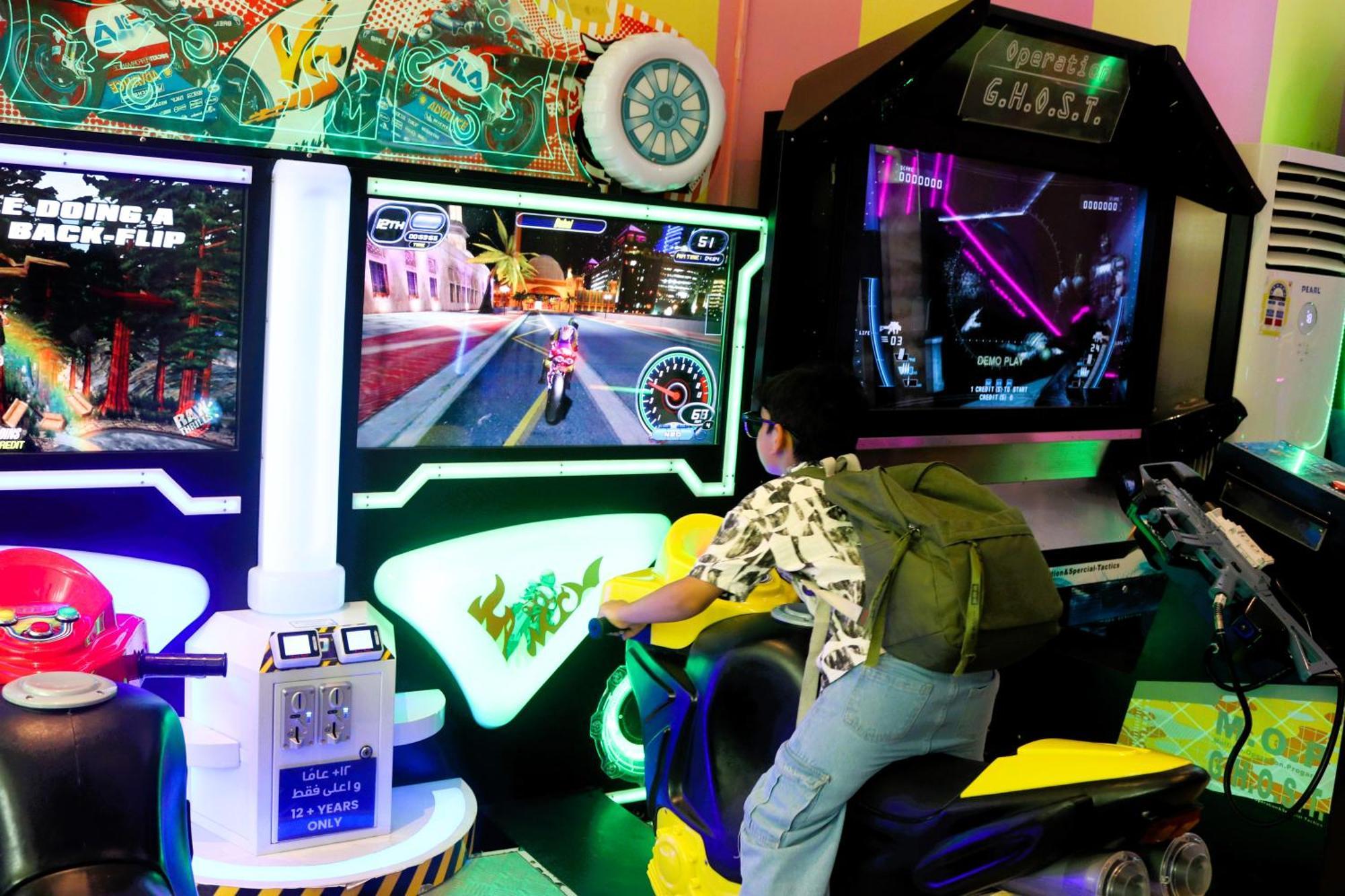 泻湖畔豪华spa度假村 麦纳麦 外观 照片 The photo shows a person playing an arcade motorcycle racing game. They are seated on a motorcycle-shaped seat, actively engaging with the game displayed on the screen in front of them. The screen shows a vibrant racing scene with streets and colorfu