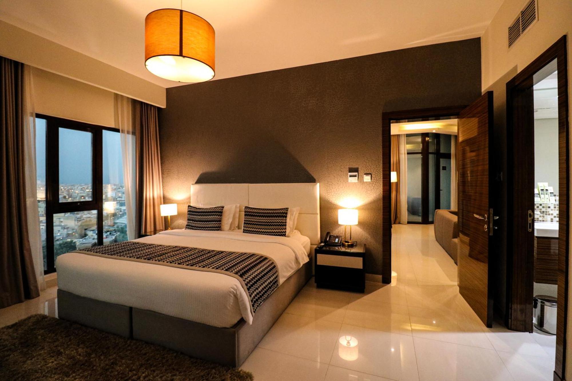 泻湖畔豪华spa度假村 麦纳麦 外观 照片 The photo depicts a modern hotel room or suite. It features a large bed with a white and gray color scheme, accented with decorative pillows. On either side of the bed, there are sleek bedside lamps providing warm lighting. The walls are a dark color