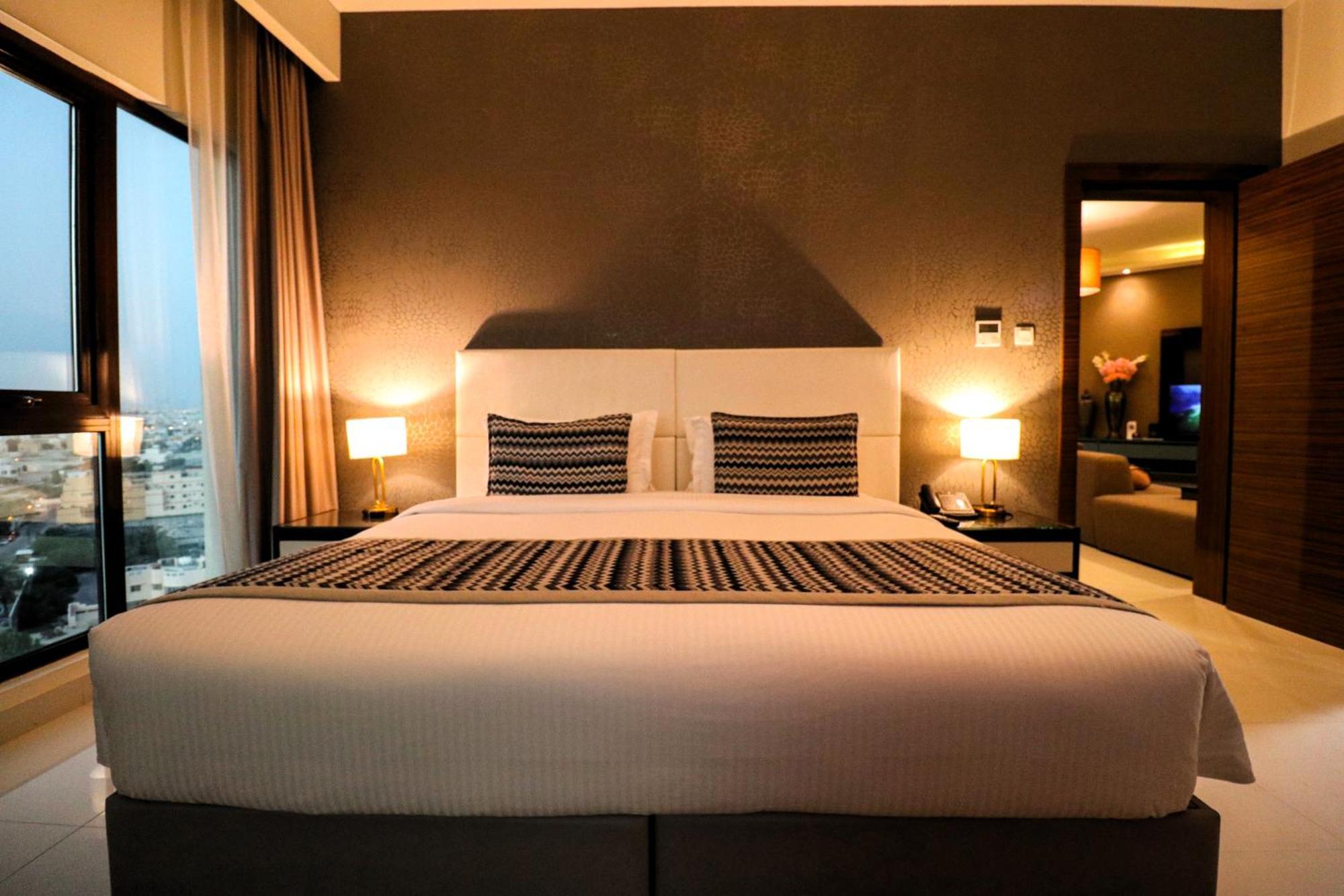 泻湖畔豪华spa度假村 麦纳麦 外观 照片 The photo depicts a modern hotel room featuring a large bed with a white comforter and two decorative pillows. The headboard is light-colored, and the walls are painted a dark hue. On either side of the bed, there are bedside tables with lamps. The r