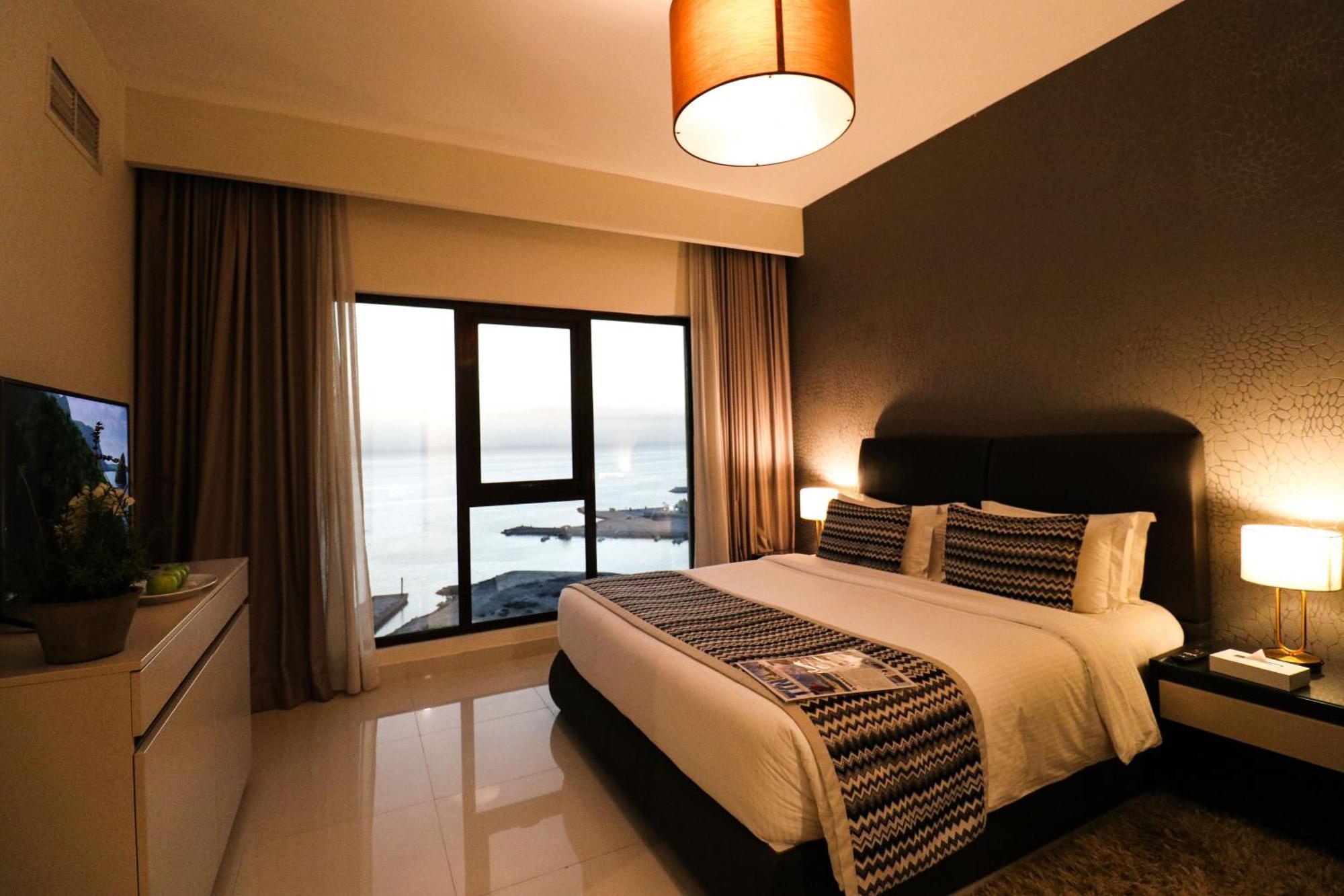 泻湖畔豪华spa度假村 麦纳麦 外观 照片 The photo shows a modern hotel room featuring a neatly made bed with decorative pillows. The room has a stylish design with a dark accent wall and a large window that offers a view of the outdoors. Natural light comes in, giving the space a bright an