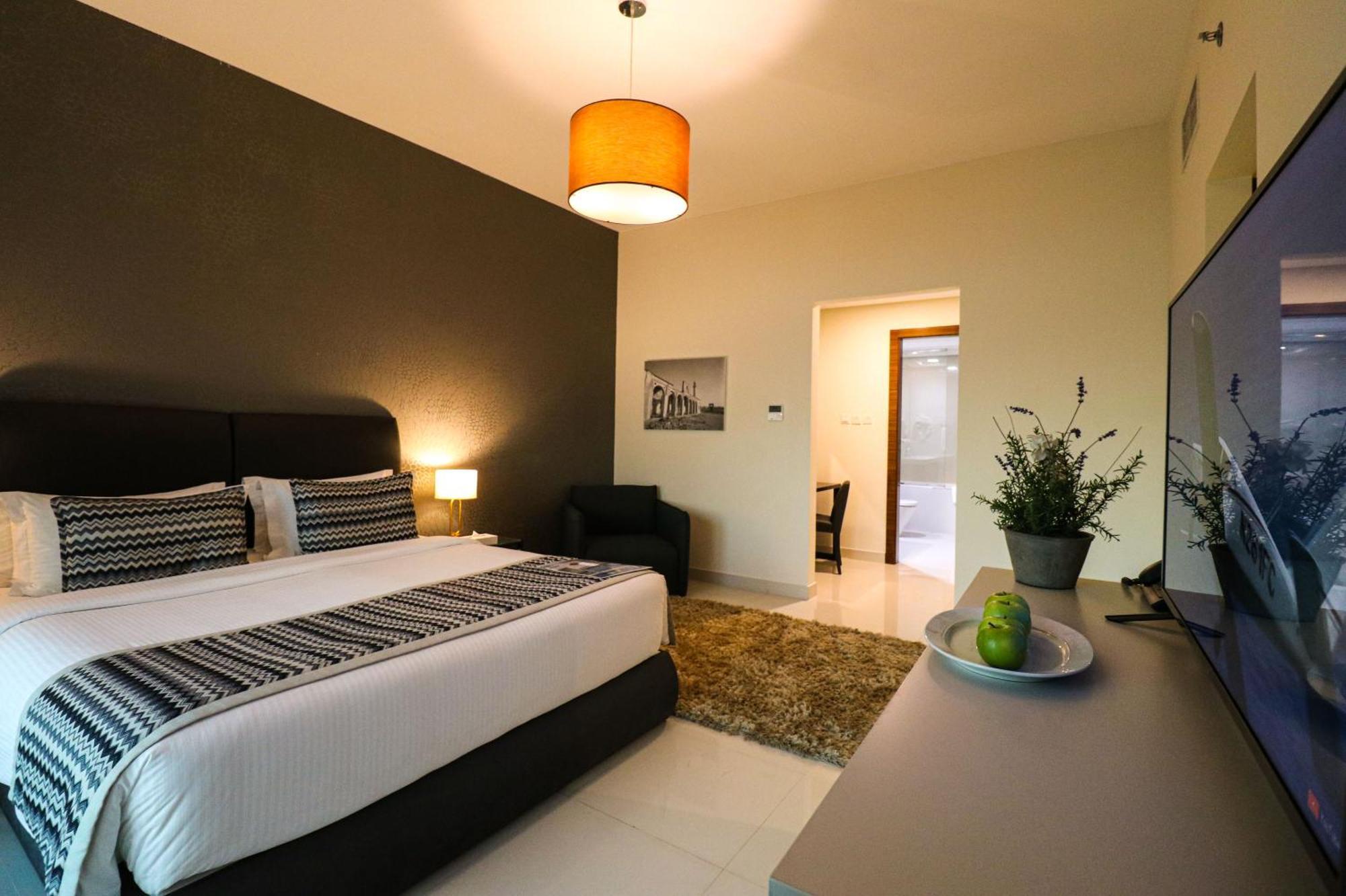 泻湖畔豪华spa度假村 麦纳麦 外观 照片 The photo shows a modern hotel room. It features a large bed with a neatly made white and dark-colored duvet. On either side of the bed, there are bedside tables with lamps. The wall behind the bed is painted in a dark color, creating a contrast with
