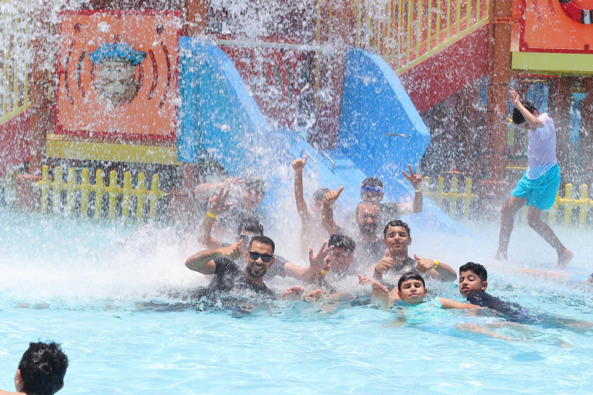 泻湖畔豪华spa度假村 麦纳麦 外观 照片 The photo shows a lively scene at a water park or pool area. Several people, including adults and children, are enjoying themselves in the water, splashing and posing for the camera. Water is cascading down, creating a refreshing atmosphere. In the b