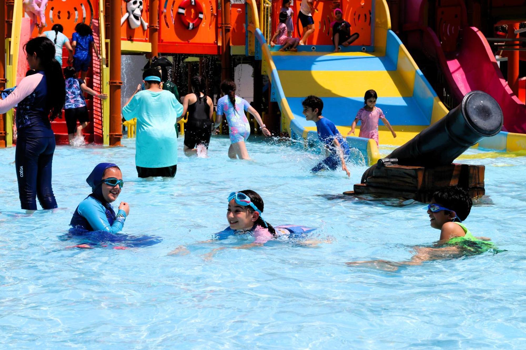 泻湖畔豪华spa度假村 麦纳麦 外观 照片 The photo shows a vibrant water park scene with several children playing in a shallow pool. Some are swimming and splashing around, while others are playing on colorful slides in the background. The atmosphere is lively and cheerful, with kids of var