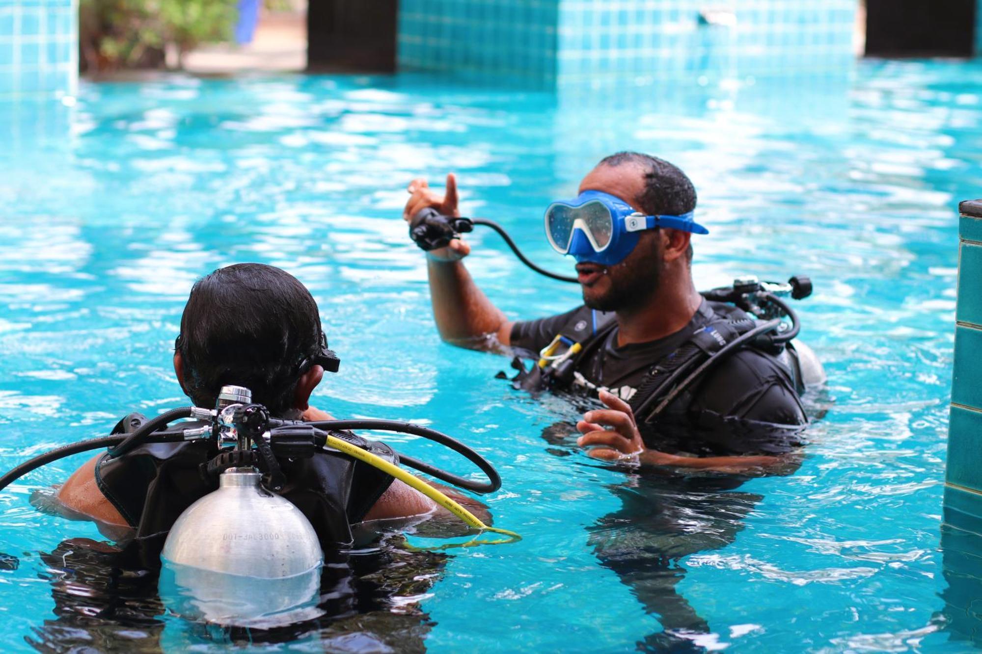 泻湖畔豪华spa度假村 麦纳麦 外观 照片 The photo shows two divers in a pool. One diver is wearing a scuba mask and is speaking to the other diver, who is also equipped with scuba gear. They appear to be engaged in a discussion, possibly related to diving instructions or safety. The water 