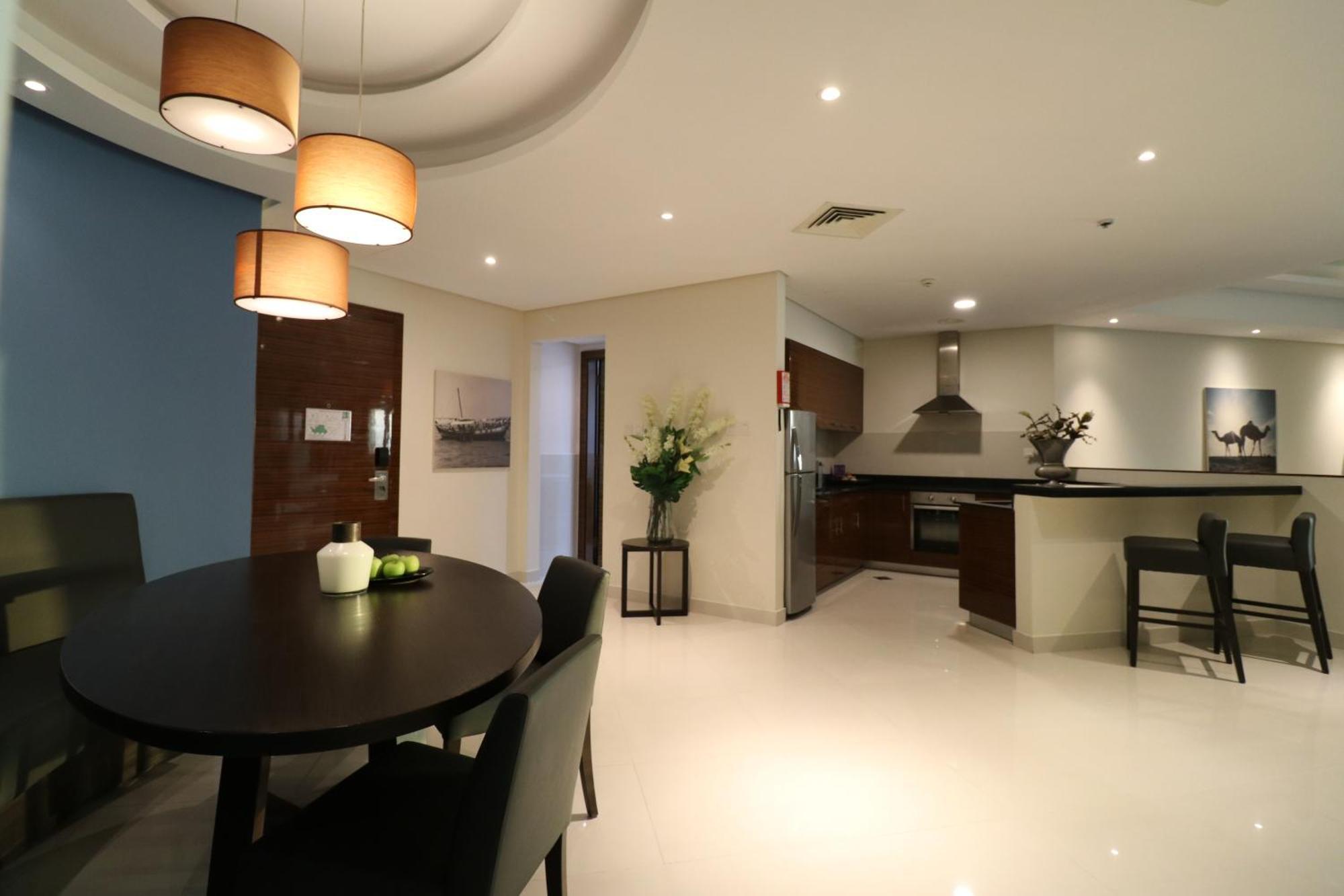 泻湖畔豪华spa度假村 麦纳麦 外观 照片 The photo shows a modern, open-concept dining and kitchen area. On the left, there is a round dining table with black chairs, accompanied by a few decorative elements like a small vase and some fruit. The walls have a combination of light and dark to