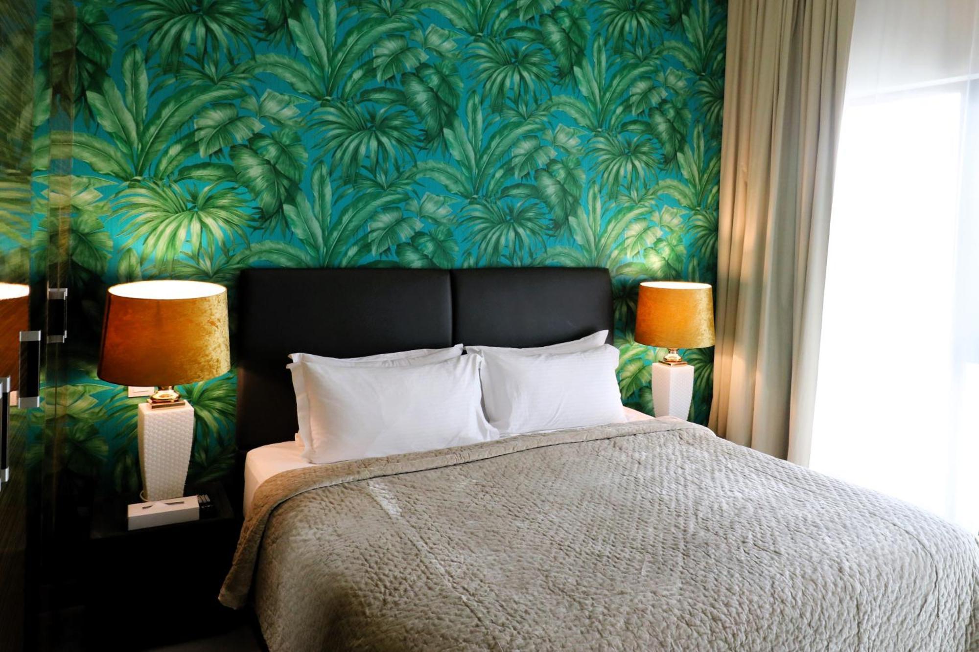 泻湖畔豪华spa度假村 麦纳麦 外观 照片 The photo shows a stylish bedroom featuring a large bed with white pillows and a gray blanket. The headboard is upholstered in black, providing a modern touch. Behind the bed, there is a vibrant green wallpaper with a tropical leaf pattern, adding a 