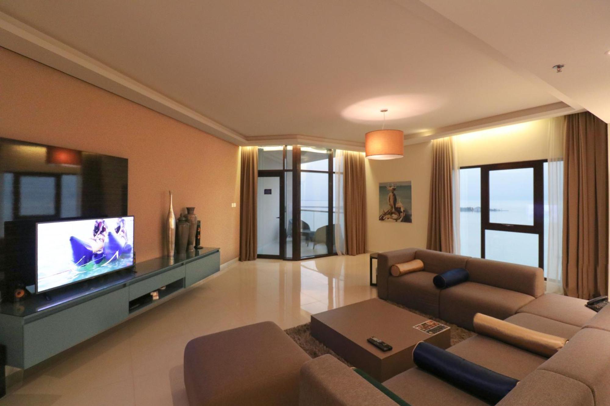泻湖畔豪华spa度假村 麦纳麦 外观 照片 The photo shows a modern living room with a sleek design. There is a large wall-mounted television on a contemporary entertainment unit, with decorative items placed beside it. The room features a comfortable sectional sofa in light tones, with a cof
