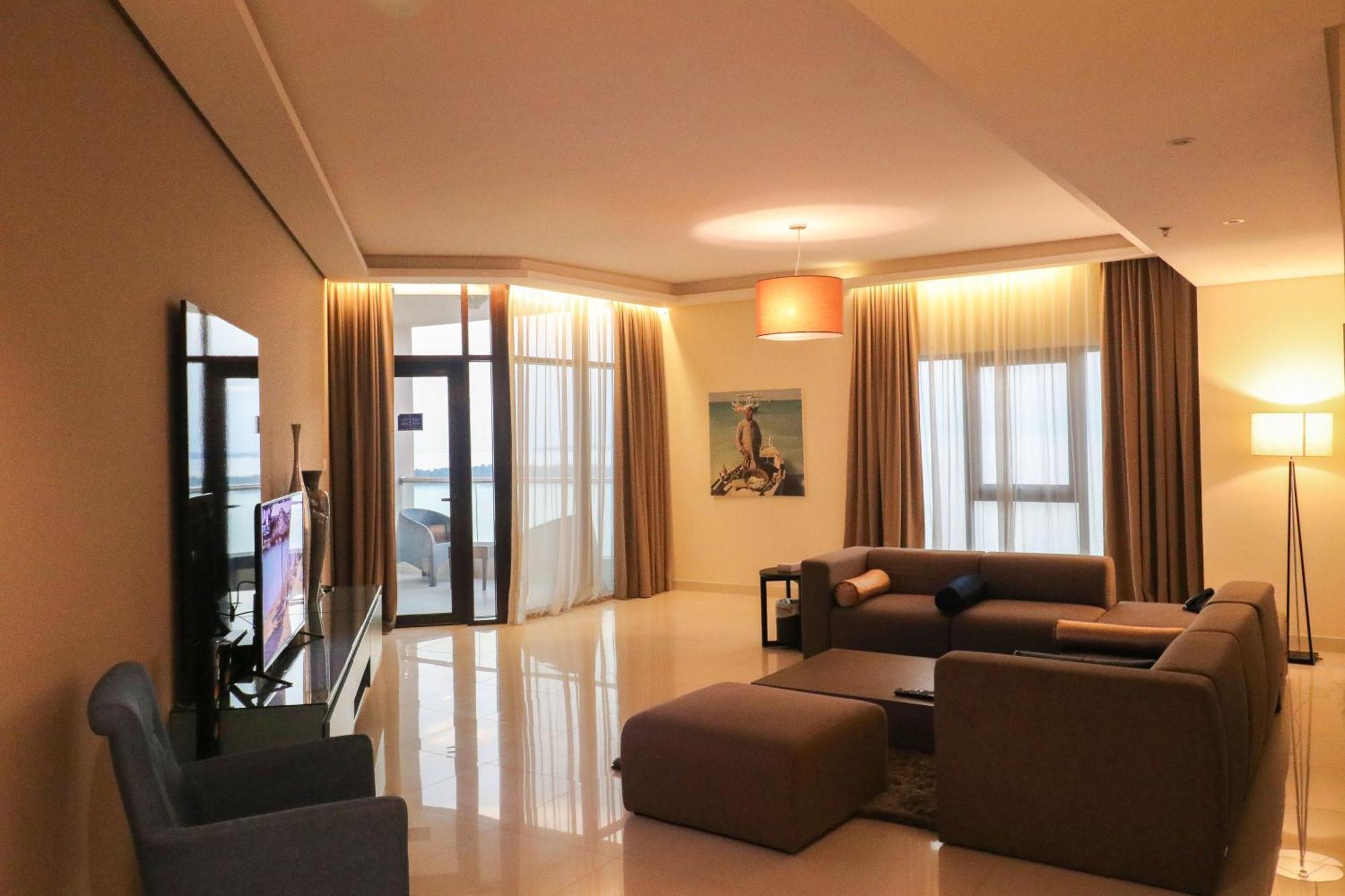 泻湖畔豪华spa度假村 麦纳麦 外观 照片 The photo shows a modern living room with a spacious and elegant design. It features a large couch in neutral tones, a soft ottoman, and a stylish coffee table. The walls are painted in a light color, and there are large windows with sheer curtains a