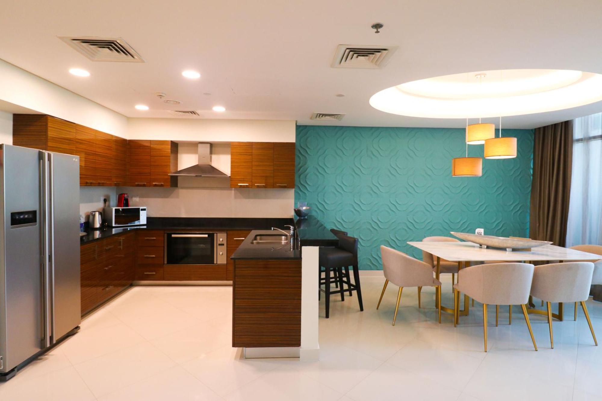 泻湖畔豪华spa度假村 麦纳麦 外观 照片 The photo shows a modern kitchen and dining area. The kitchen features wooden cabinets, sleek appliances including a stainless steel refrigerator, microwave, and an oven. There is a dark countertop and a small breakfast bar with high stools. The wall